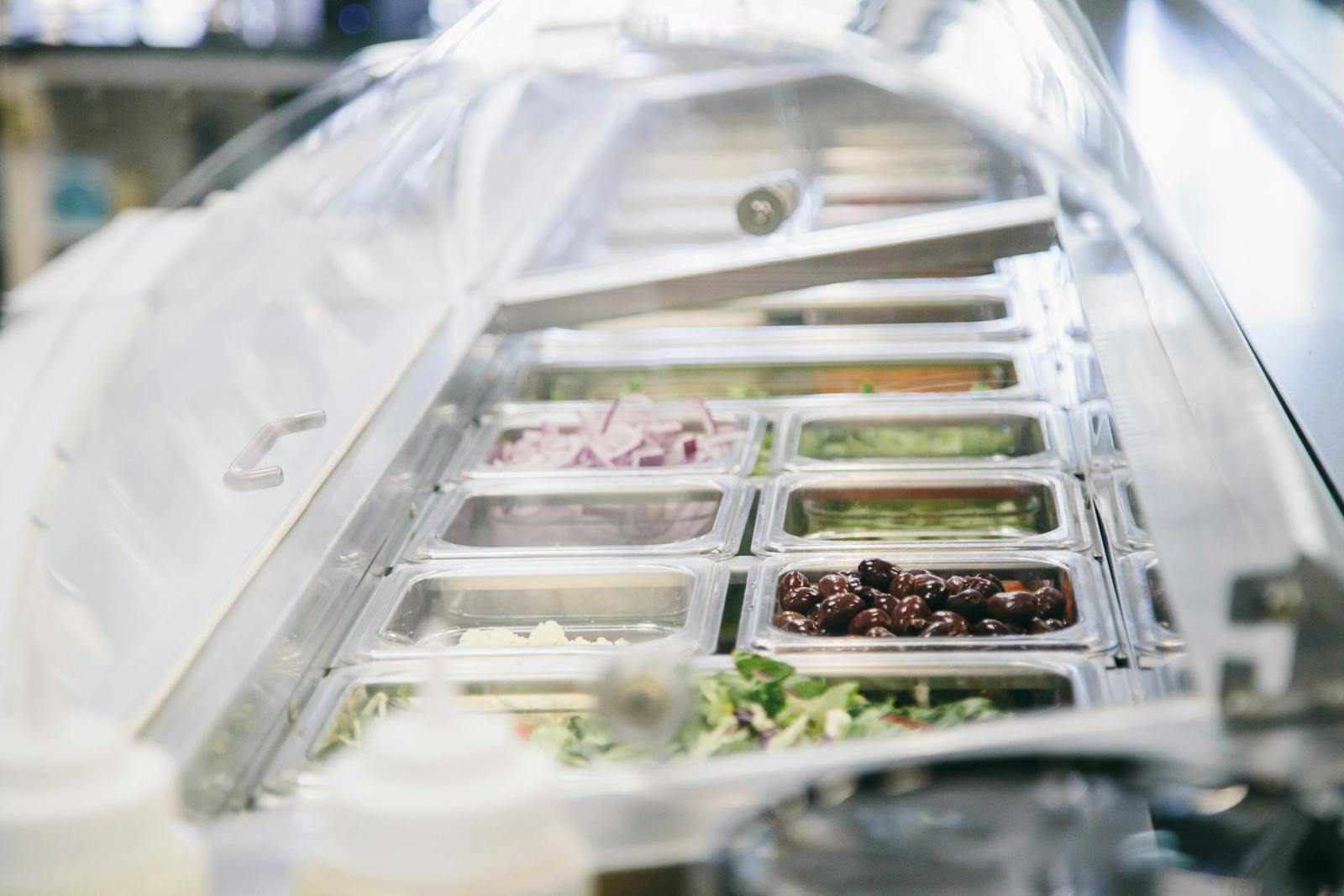 Fresh vegetables, olives, and toppings arranged at the service counter