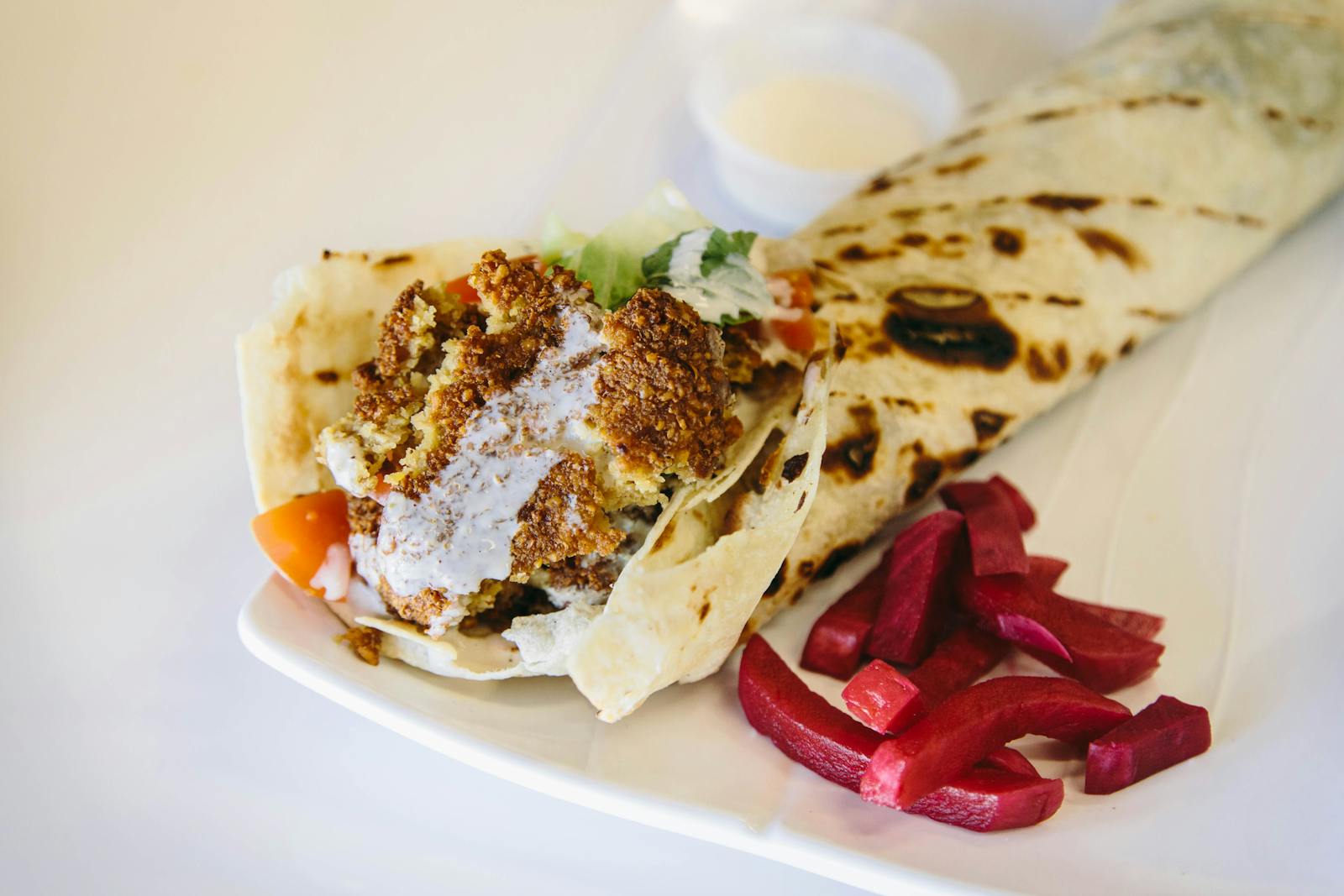 Falafel wrap with pickled turnips and house sauce served on a white plate
